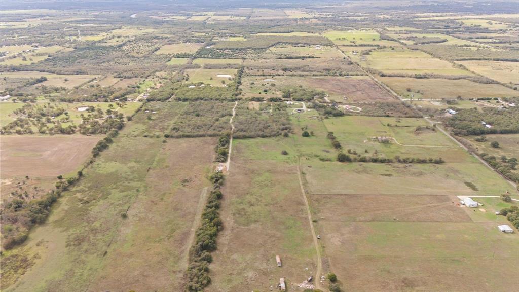 Aerial perspective of expansive acreage featuring open pastureland, clusters of mature trees, and unpaved access paths