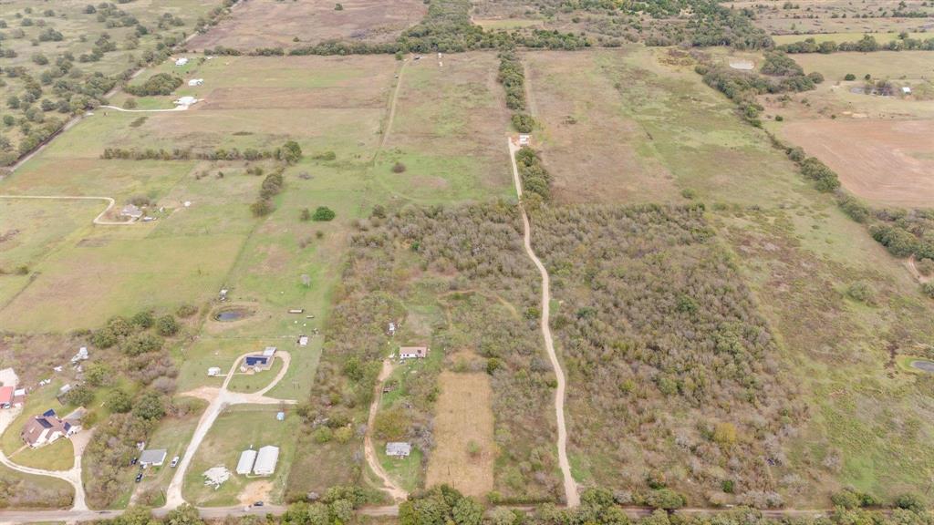 Expansive acreage featuring cleared pasture land, clusters of mature trees, natural water features, and an unpaved access path