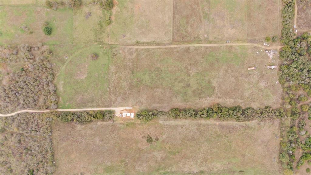 Aerial perspective of expansive acreage featuring open pasture land, dense mature tree clusters, and a gravel access road Aerial perspective of expansive acreage featuring open pasture land, dense mature tree clusters, and a gravel access road