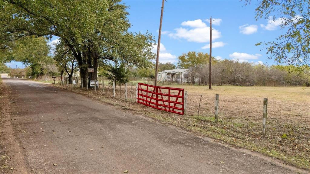 Expansive acreage featuring mature trees, perimeter wire fencing, and a red metal swing gate