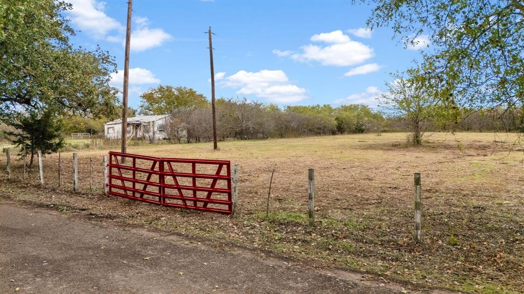 Expansive level lot featuring a red metal tube gate, wire perimeter fencing, and mature trees