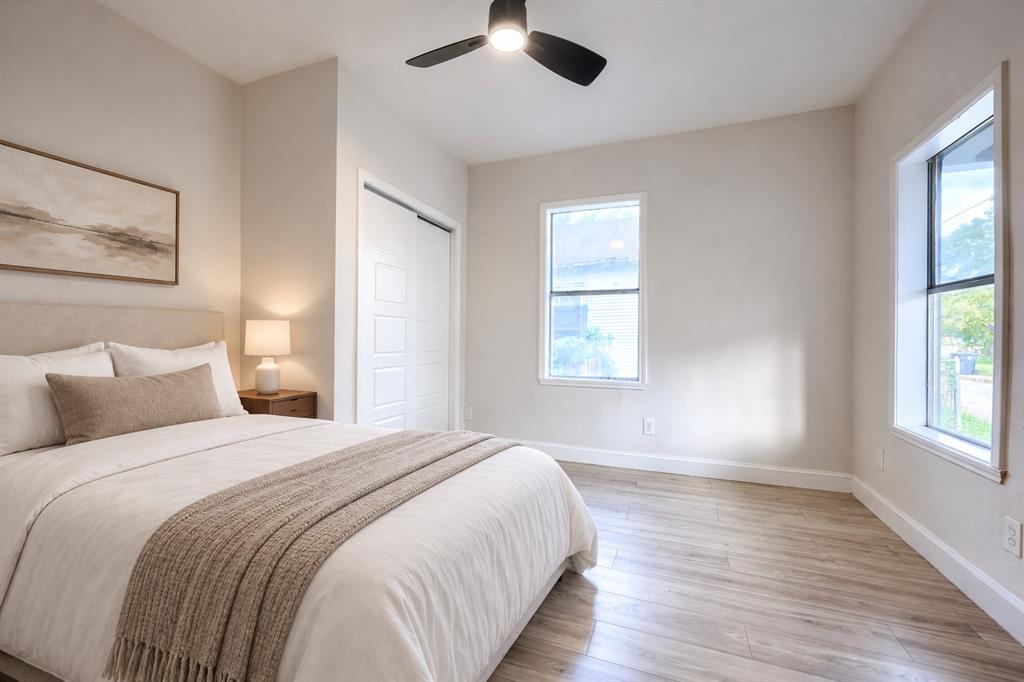 Neutral interior featuring wood-finish flooring, crisp white trim, two windows, and a matte black ceiling fan with integrated lighting
