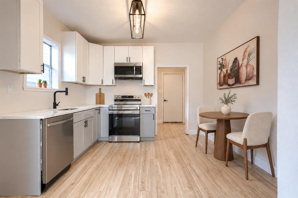 Kitchen featuring white upper cabinetry, grey lower cabinetry, stainless steel appliances, light-toned wood-finish flooring, and a geometric pendant light fixture