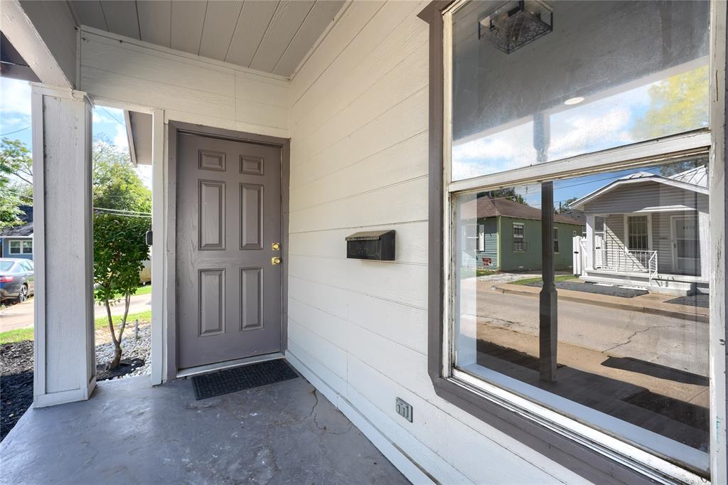 Covered entryway featuring horizontal lap siding, a paneled door, a large fixed-pane window with dark trim, and a wall-mounted metal mailbox