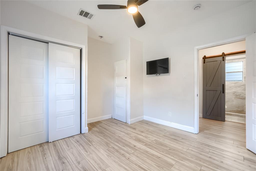 Interior space featuring wood-finish flooring, a ceiling fan with integrated lighting, sliding closet doors, and a grey sliding barn door