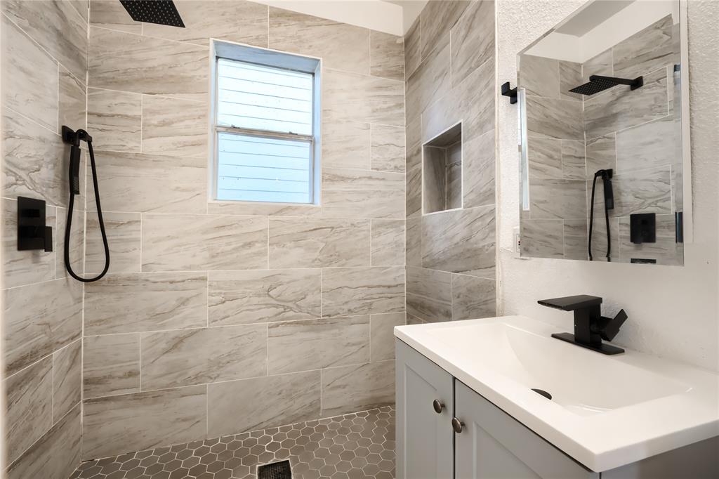 Bathroom featuring large-format neutral-toned wall tile, a built-in recessed shower niche, hexagonal floor tiling, a vanity with a solid-surface countertop, and matte black plumbing fixtures