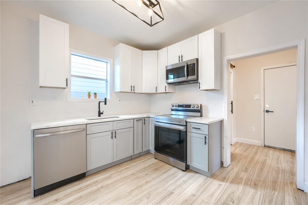 Kitchen featuring white upper cabinetry, grey lower cabinetry, stainless steel appliances, stone-look countertops, and wood-finish flooring