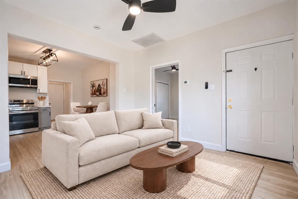 Wood-finish flooring, ceiling fan with integrated lighting, kitchen featuring stainless steel appliances and white cabinetry, and multi-panel entry door