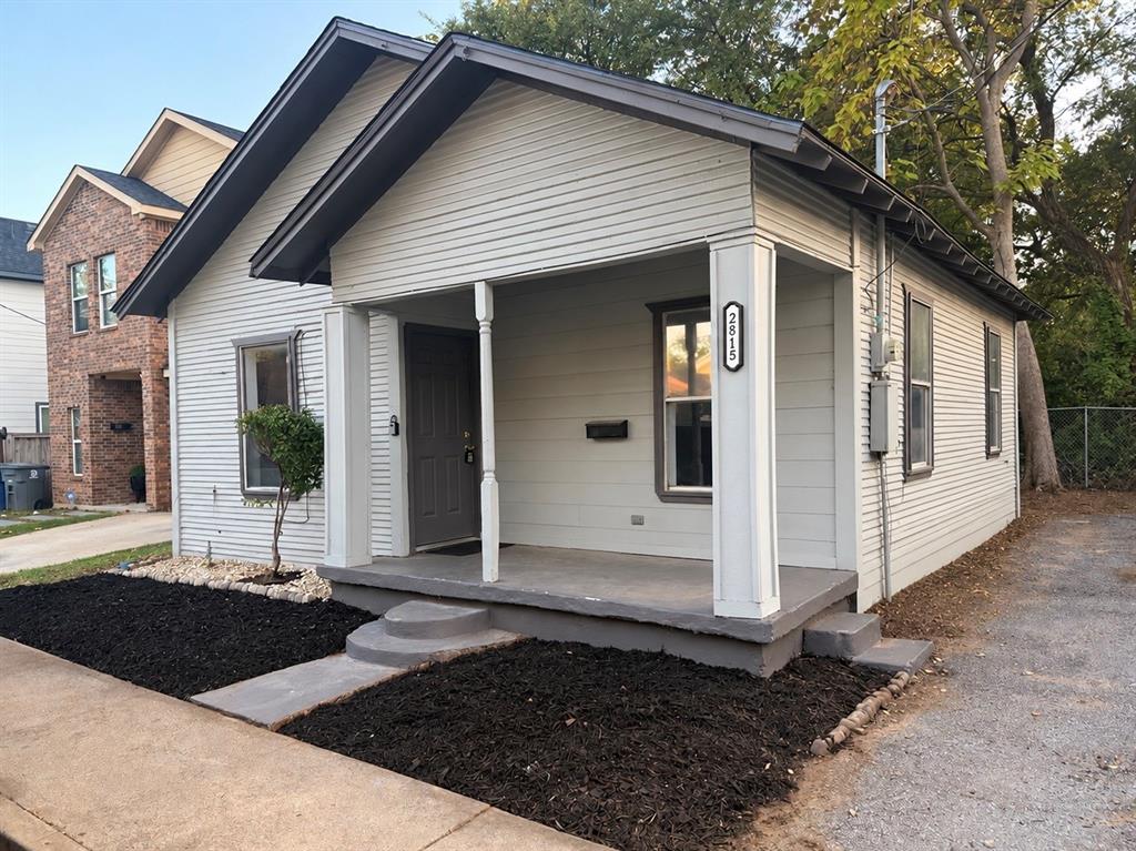 Single-story exterior featuring light-toned horizontal siding, a covered front porch with square columns, and a gable roofline