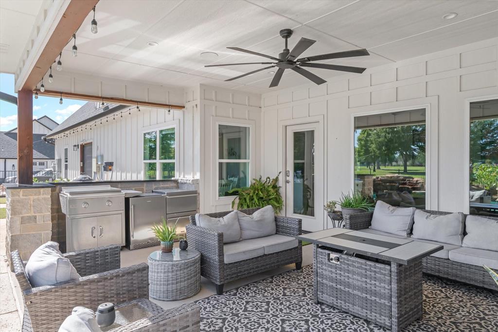 Covered patio featuring board and batten siding, a stone-base outdoor kitchen with built-in stainless steel appliances, recessed ceiling lighting, and a multi-blade ceiling fan