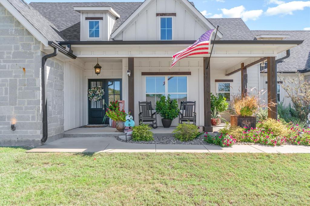 Modern farmhouse exterior featuring vertical board-and-batten siding, natural stone veneer accents, a covered front porch with timber posts, and a dark-framed glass paneled front door Modern farmhouse exterior featuring vertical board-and-batten siding, natural stone veneer accents, a covered front porch with timber posts, and a dark-framed glass paneled front door