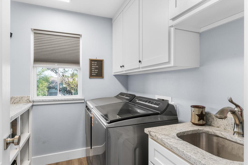 Laundry area featuring light-toned stone countertops, white shaker-style cabinetry, an integrated stainless steel basin with a gooseneck faucet, and wood-finish flooring