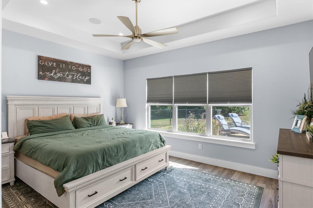 Tray ceiling featuring recessed lighting and a central ceiling fan, expansive triple-pane window, and wood-finish flooring
