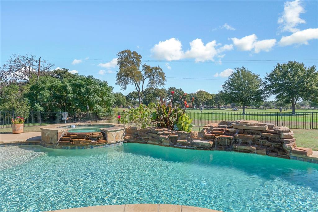 In-ground swimming pool featuring a stacked stone waterfall, integrated spill-over spa, and perimeter wrought-iron fencing