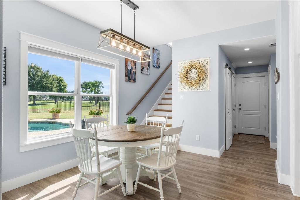 Wood-finish flooring, rectangular multi-light pendant fixture, staircase with wood handrail, and large window with exterior pool visibility