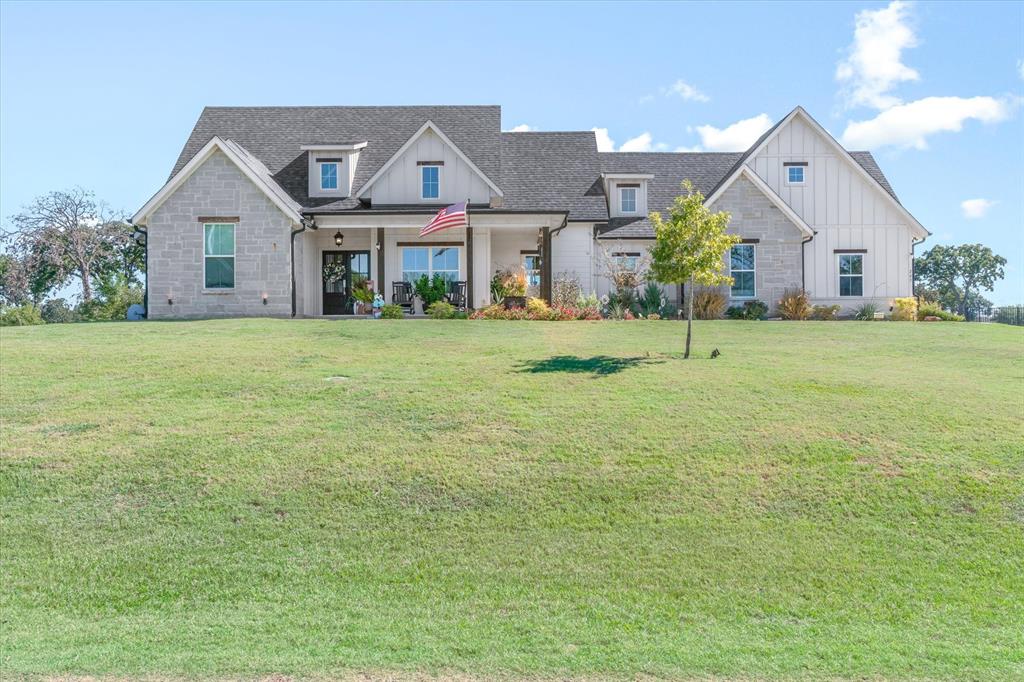 Multi-gabled exterior featuring light-toned stone masonry, vertical board-and-batten siding, a covered front porch with timber support columns, and expansive front lawn Multi-gabled exterior featuring light-toned stone masonry, vertical board-and-batten siding, a covered front porch with timber support columns, and expansive front lawn