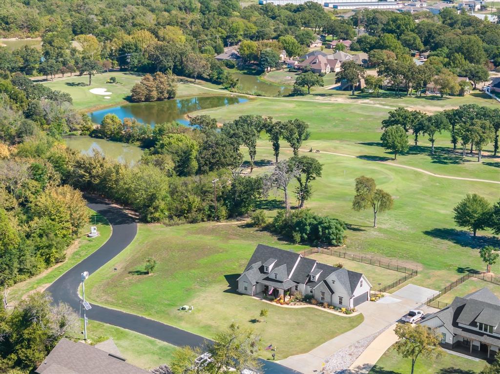 Aerial perspective featuring a multi-gabled residence with a paved driveway, expansive lawn, and direct exposure to a golf course landscape with water features and mature trees Aerial perspective featuring a multi-gabled residence with a paved driveway, expansive lawn, and direct exposure to a golf course landscape with water features and mature trees