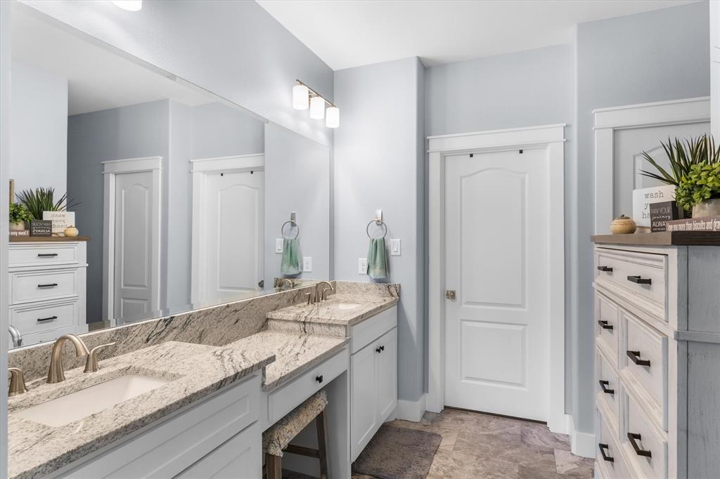 Dual-sink vanity with stone countertop, undermount basins, expansive wall-to-wall mirror, and neutral-toned tile flooring