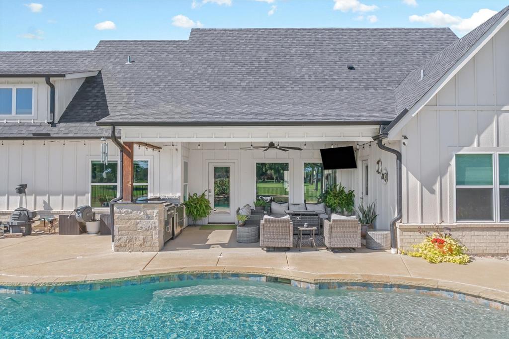 Covered outdoor living area featuring a stone-clad built-in kitchen, ceiling fan, hardscaped patio, and an in-ground swimming pool