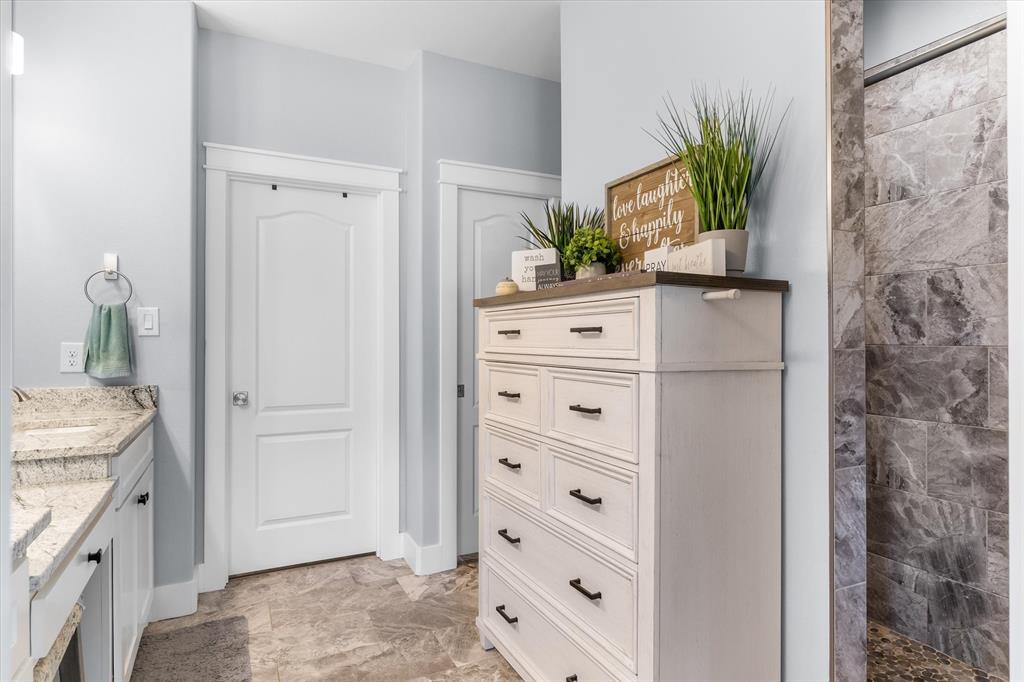 Stone tile flooring, vanity with stone countertop, and tiled shower enclosure