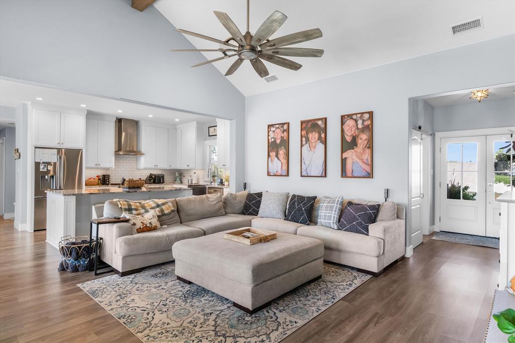Vaulted ceiling featuring an expansive multi-blade ceiling fan, wood-finish flooring, and white cabinetry with stainless steel appliances