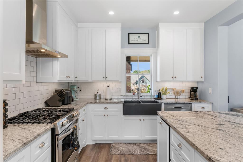 Kitchen featuring white shaker-style cabinetry, stone countertops, farmhouse-style sink, stainless steel chimney range hood, and subway tile backsplash