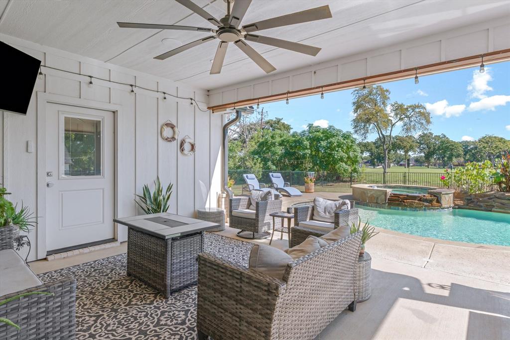 Covered patio with board-and-batten siding and a ceiling fan, featuring a swimming pool with a stone-accented water feature