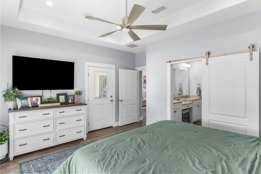 Tray ceiling with a multi-blade ceiling fan, wood-finish flooring, and white paneled sliding barn door