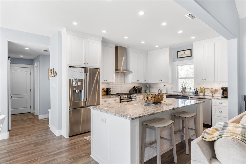 Kitchen featuring white shaker-style cabinetry, stone countertops, stainless steel appliances, a tiled backsplash, and recessed lighting