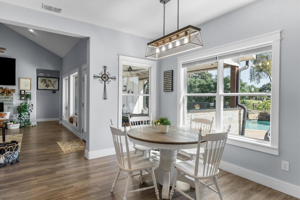 Dining area featuring wood-finish flooring, vaulted ceilings, multi-light rectangular pendant fixture, and large windows with outdoor pool exposure