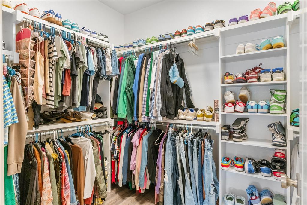 Custom walk-in closet featuring multi-level hanging rods, tiered built-in shelving, and wood-finish flooring