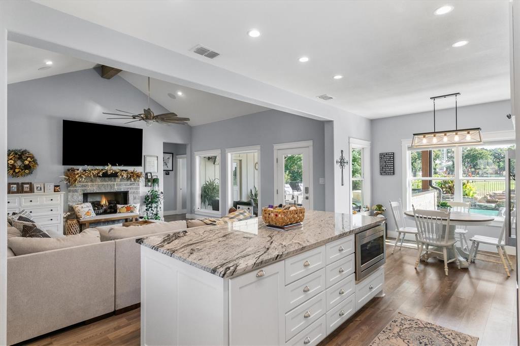 Open-concept kitchen and living area featuring a large center island with stone countertop, vaulted ceilings with recessed lighting, and a stone-surround fireplace