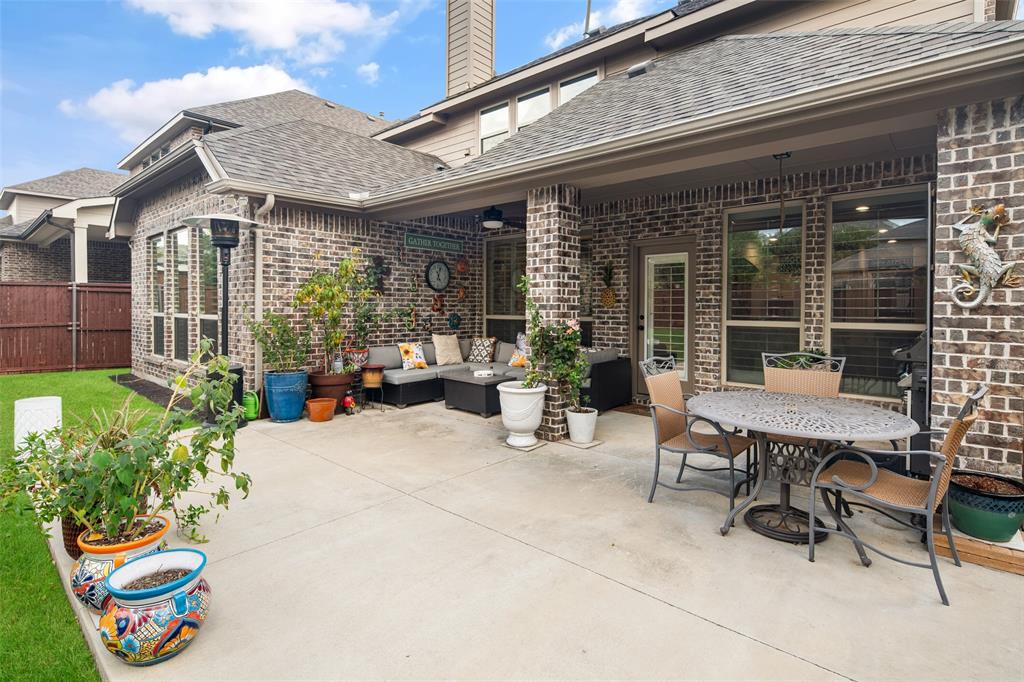 Covered concrete patio featuring a brick exterior facade, ceiling fan, and fenced lawn