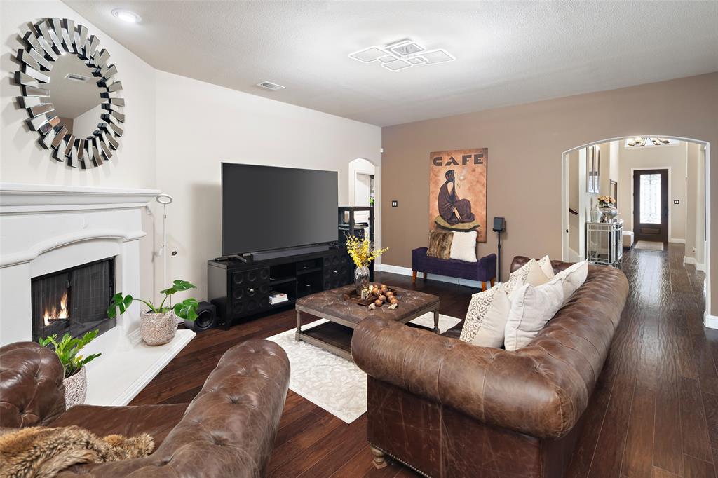 Living area featuring a white fireplace mantle, wood-finish flooring, recessed lighting, a modern geometric ceiling fixture, and an arched entry