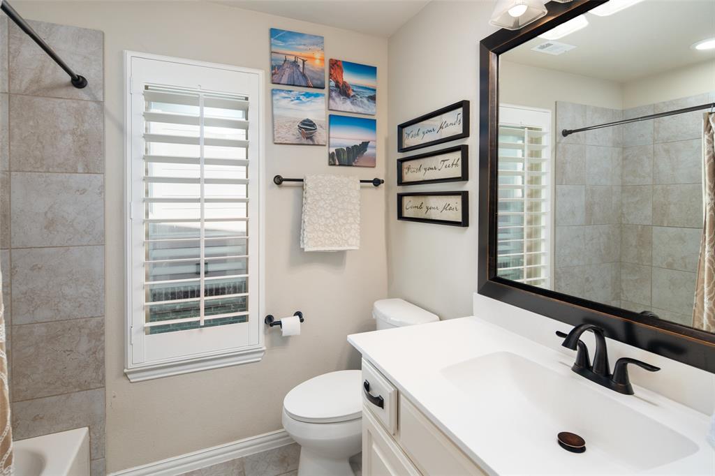 Bathroom featuring a vanity with a solid-surface countertop, rectangular undermount sink, and matte black hardware, accompanied by plantation shutters and wall-surround tile