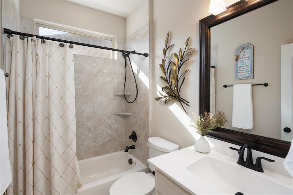 Bathroom featuring a white vanity with a rectangular sink, matte black faucet, stone-patterned tile tub surround, and a transom window
