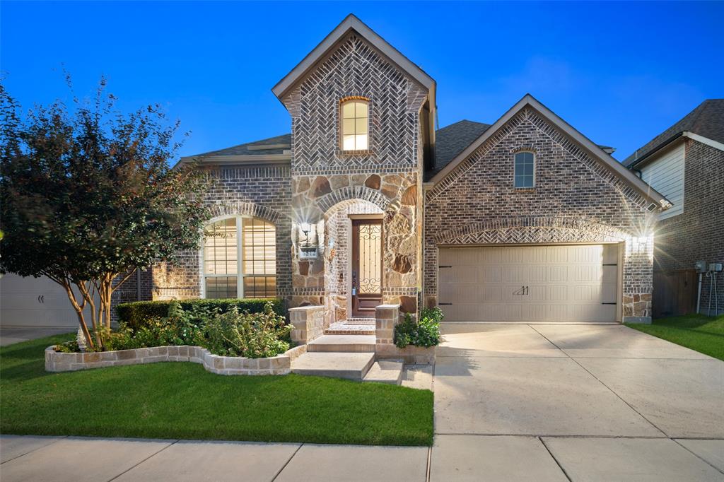 Multi-gabled brick and stone exterior featuring a herringbone-patterned gable peak, arched masonry entryway, leaded glass front door, and a concrete driveway