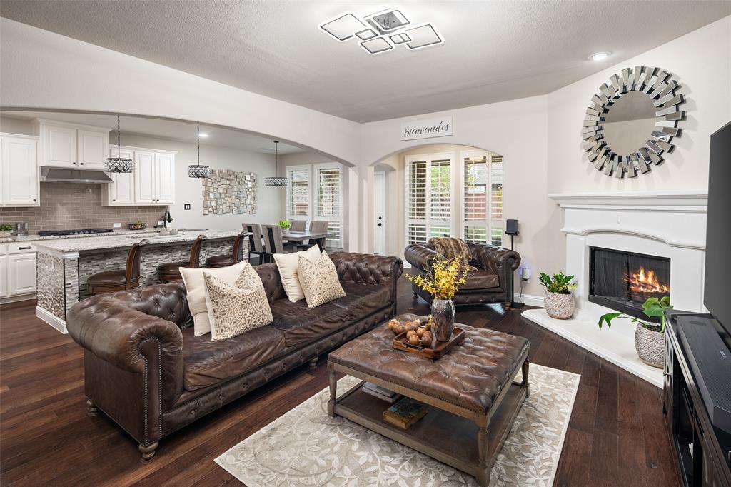 Open-concept living space featuring wood-finish flooring, a fireplace with a decorative mantel, white cabinetry, a kitchen island with a stone-finish countertop, and recessed ceiling lighting