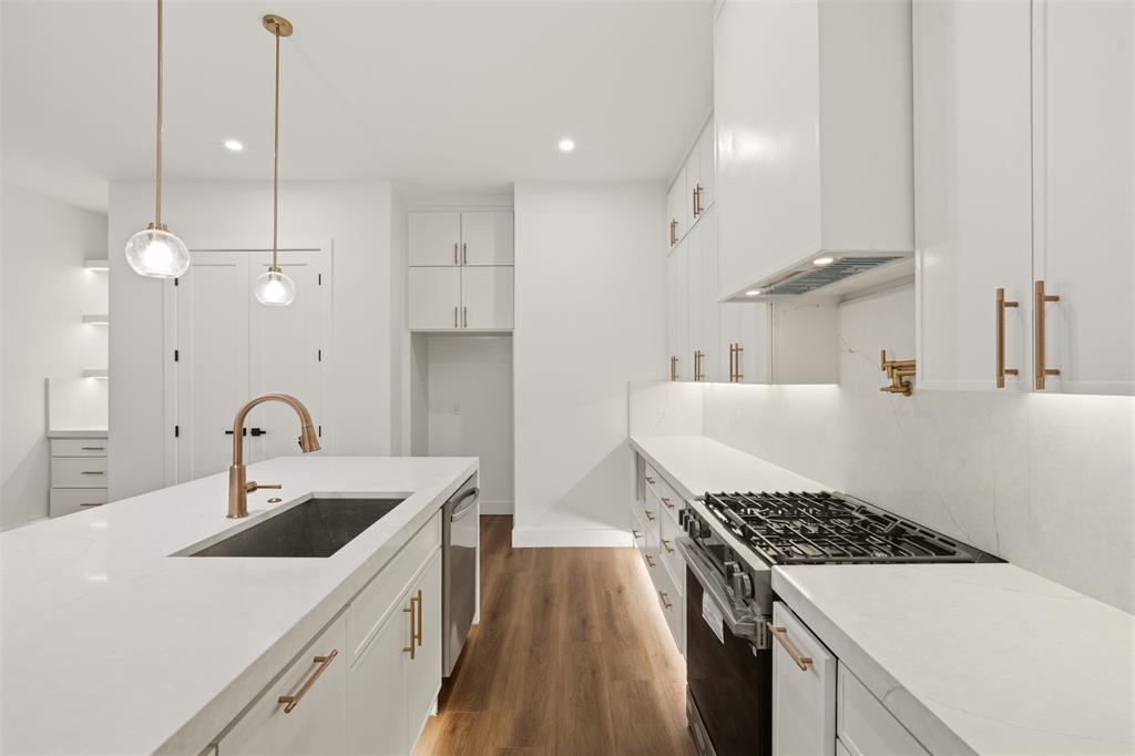 Kitchen featuring white shaker cabinetry, quartz countertops, a stainless steel gas range with a matching range hood, gold-tone hardware, and wood-finish flooring