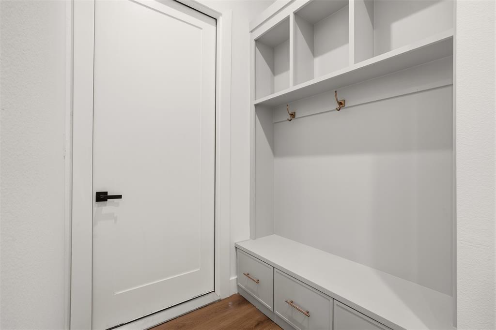 Built-in cabinetry featuring upper storage cubbies, integrated metal garment hooks, and lower drawer storage with metallic hardware, accented by a solid-core door with a matte black lever handle and wood-finish flooring