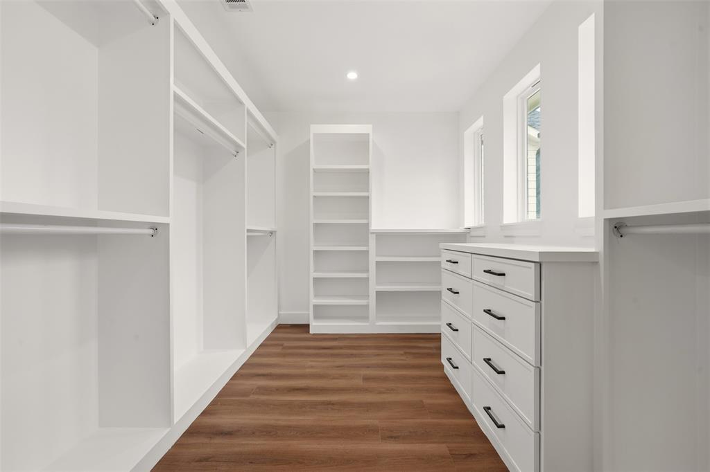 Walk-in storage space featuring white built-in cabinetry, custom shelving, integrated dresser drawers with matte black pulls, and wood-finish flooring