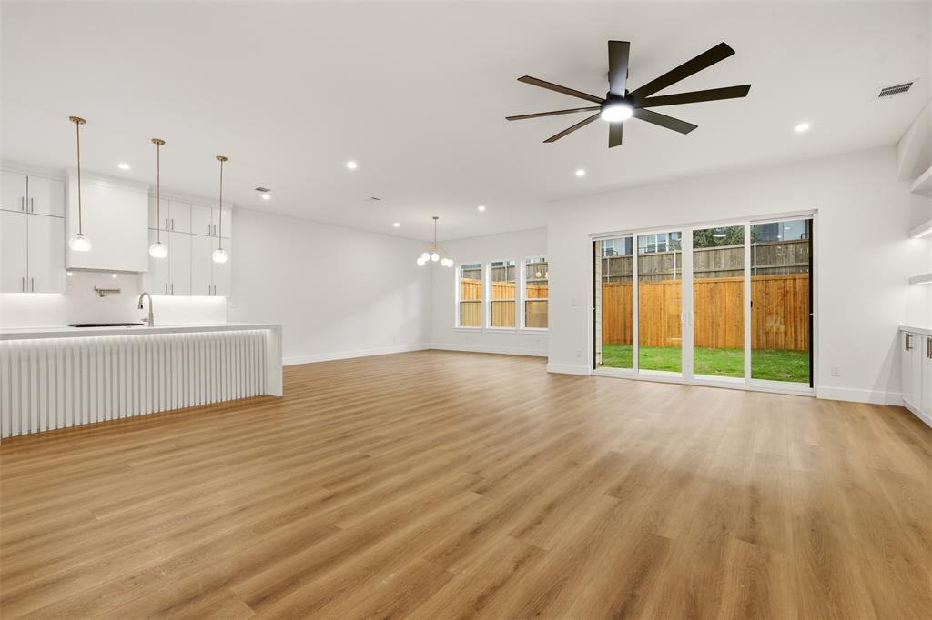 Open-concept interior featuring wood-finish flooring, a kitchen island with fluted detailing, glass sliding doors, recessed lighting, and a multi-blade ceiling fan