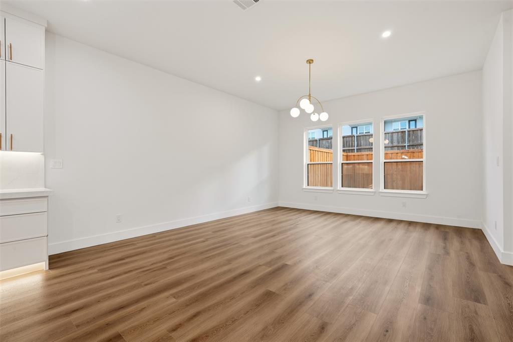 Interior space featuring wood-finish flooring, recessed lighting, a modern multi-globe chandelier, crisp white cabinetry with gold-toned hardware, and three paneled windows