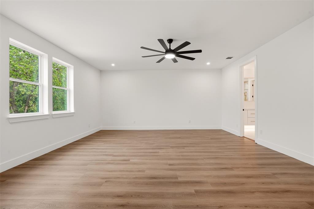 Neutral-toned interior space featuring wood-finish flooring, recessed lighting, a modern multi-blade ceiling fan with integrated light, and dual windows