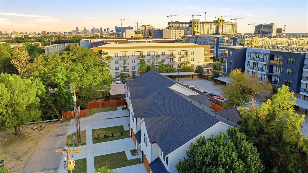 Multi-story exterior featuring a shingled roof, concrete driveway, and wood-panel garage doors, complemented by a landscaped lawn and city skyline backdrop