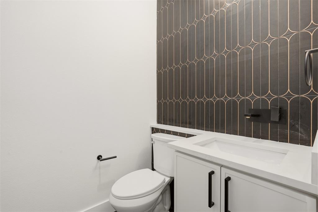 Modern vanity featuring a white countertop, under-mount sink, and matte black hardware, accented by geometric patterned wall tile and a wall-mounted faucet