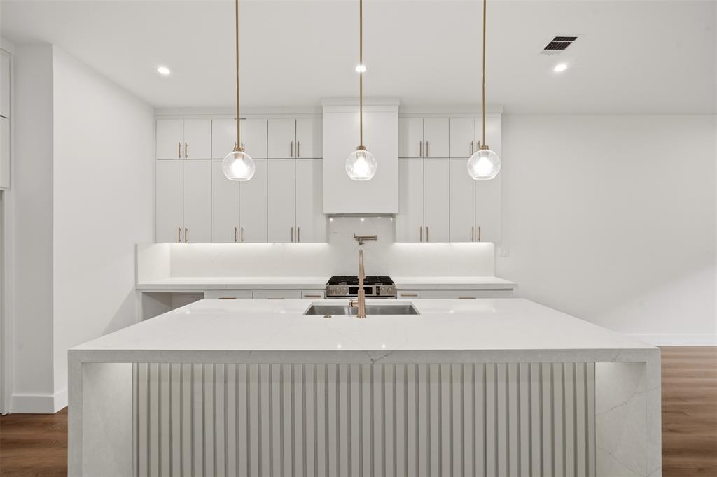 Kitchen featuring custom white cabinetry, a center island with waterfall-edge countertop and ribbed detailing, three glass pendant lights, and a stainless steel pot filler