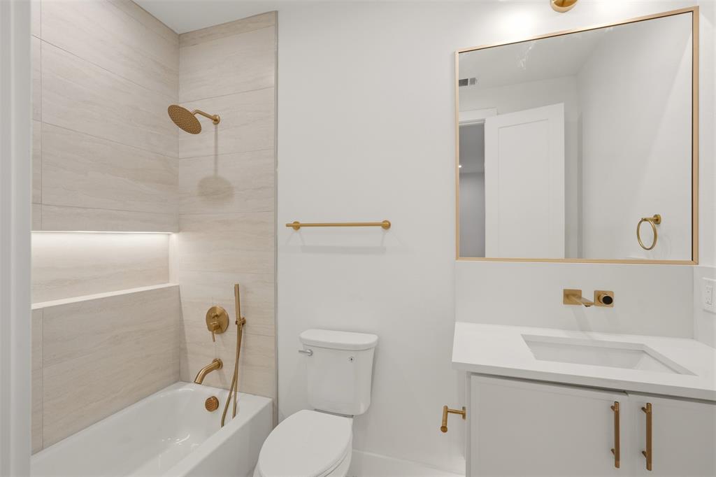 Bathroom featuring a white quartz vanity countertop, brass-finished wall-mounted faucet and hardware, undermount sink, and full-wall tub surround with integrated niche lighting