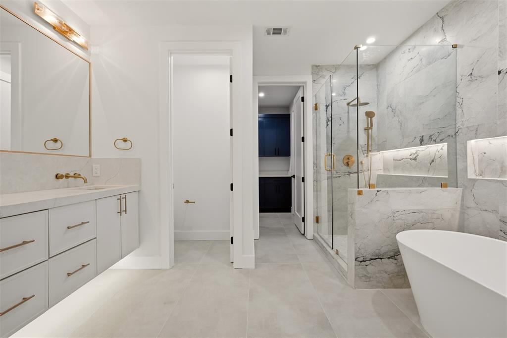 Floating vanity with stone countertop, freestanding soaking tub, glass-enclosed walk-in shower with stone surround, recessed shower niche, and brushed metallic fixtures