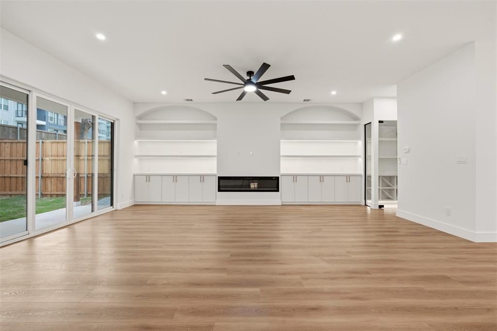 Open-concept living space featuring wood-finish flooring, a linear fireplace, arched built-in shelving, a modern ceiling fan, and sliding glass doors